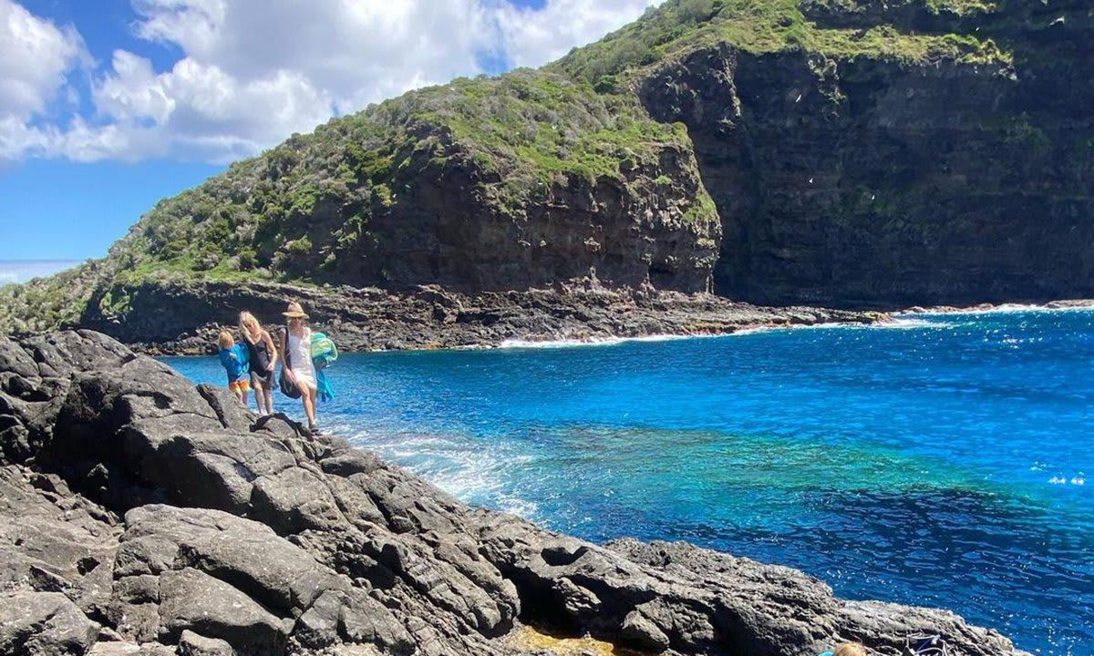 A birds eye view of the oean and natural pools. 4 people are walking over a rock bridge.