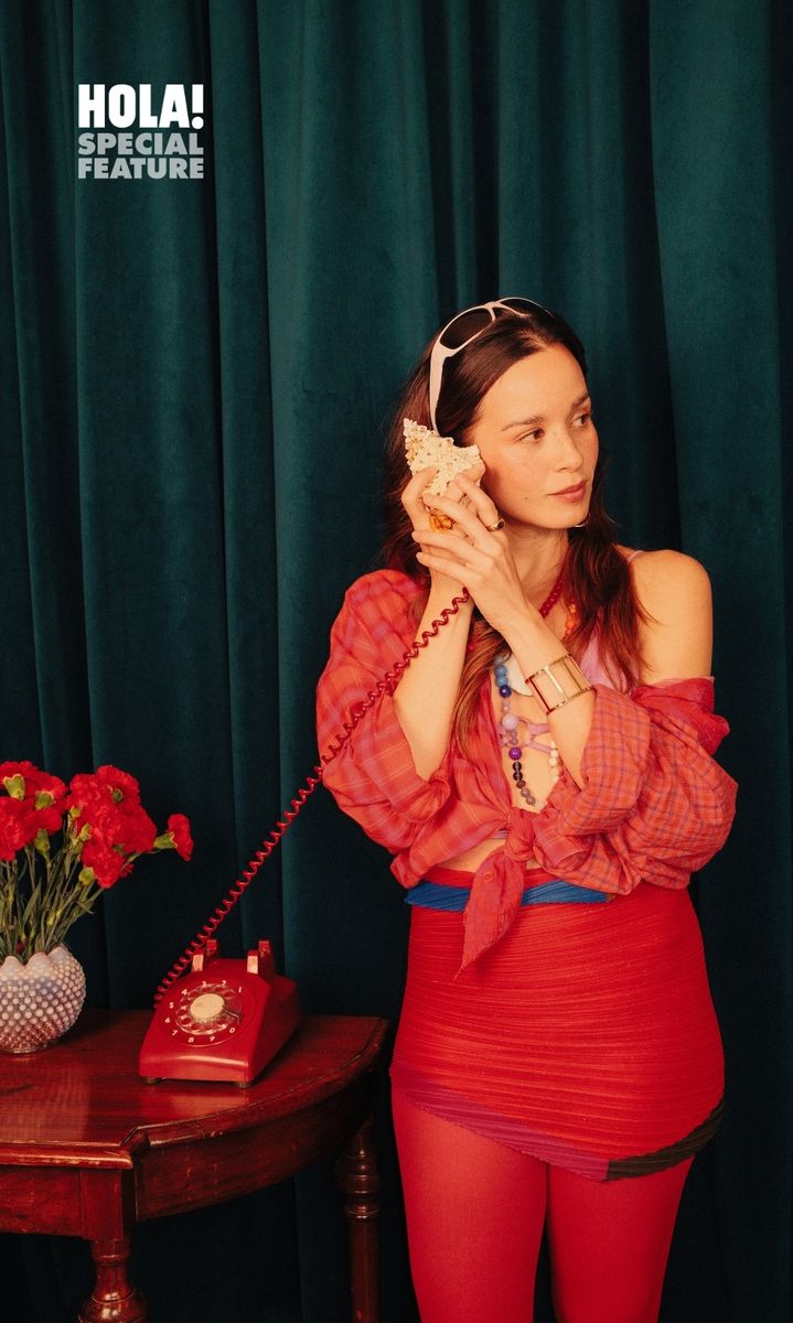 A woman in red outfit and sunglasses on head holding a phone receiver.