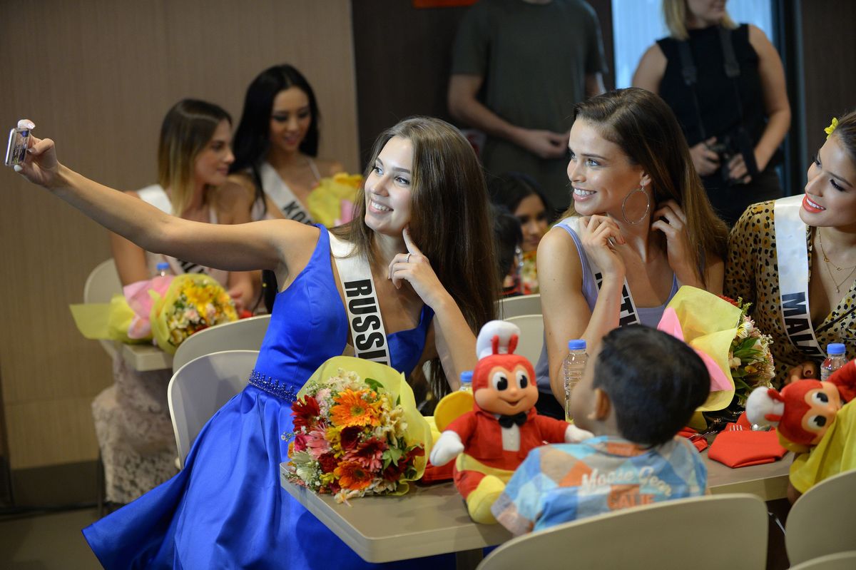  Miss Universe contestants Kseniya Alexandrova of Russia, Nicky Opheij of the Netherlands and Samantha James of Malaysia take a selfie with children from an orphanage during a visit to a popular fast food restaurant in Manila on December 7, 2017. 
Miss Universe Demi-Leigh Nel-Peters o