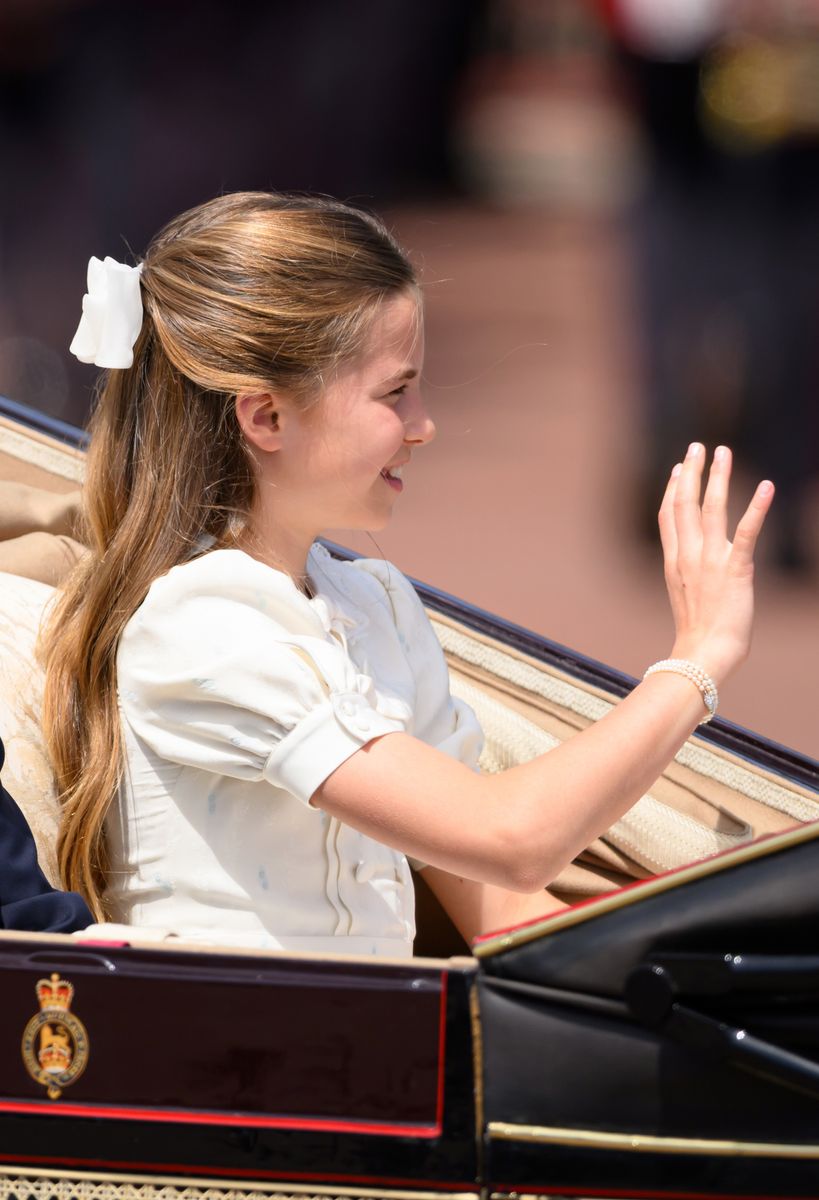 Princess Charlotte's hair was styled in a half-up look adorned with a large white bow, while soft waves flowed from mid-length to the ends.