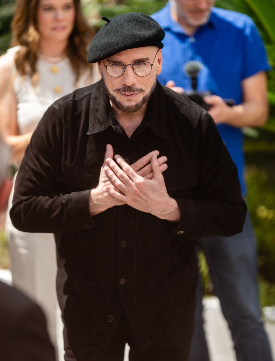 John Travolta explained that his viral berets at the 2026 Cannes Film Festival were a tribute to classic old-school directors as he promoted his directorial debut, Propeller One-Way Night Coach.