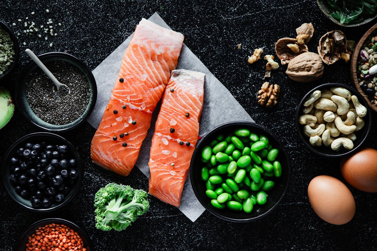 Table top view of Omega 3 rich food items on black background. Fresh raw salmon steak with beans, broccoli, lentil seeds, blueberries, chia seeds, walnuts, cashews, and brown eggs on black kitchen table.