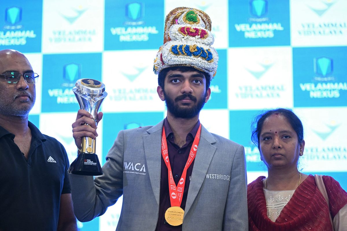 India's Gukesh Dommaraju stands beside his parents as he shows his World Chess Championship trophy during a press conference in Chennai on December 16, 2024 after his win at the FIDE World Chess Championship Singapore 2024. 