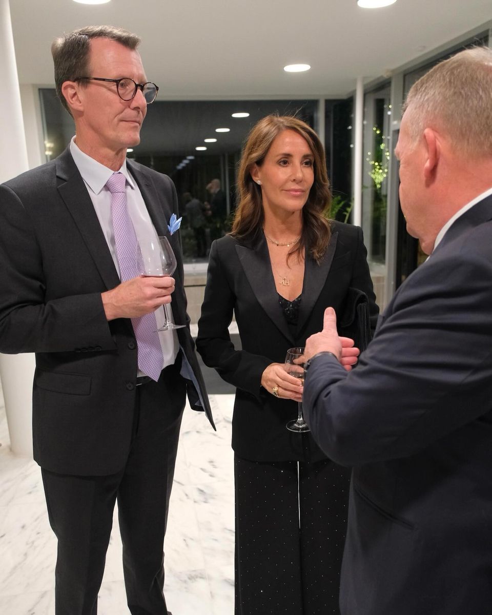 Princess Marie’s lace-trimmed top and delicate layered necklaces softened her tailored ensemble as she joined Prince Joachim in conversation with a guest.