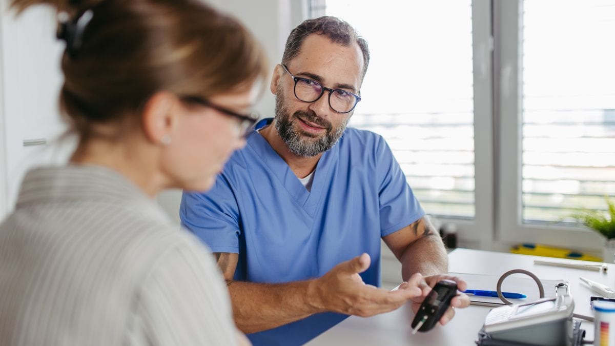 Diabetologist doctor testing blood sample on blood sugar meter in diabetes clinic. Doctor holding glucometer with test strip, waiting for results. Doctor explaining test results to patient, consulting and talking. Woman diagnosed with diabetes. Medical banner with copy space.