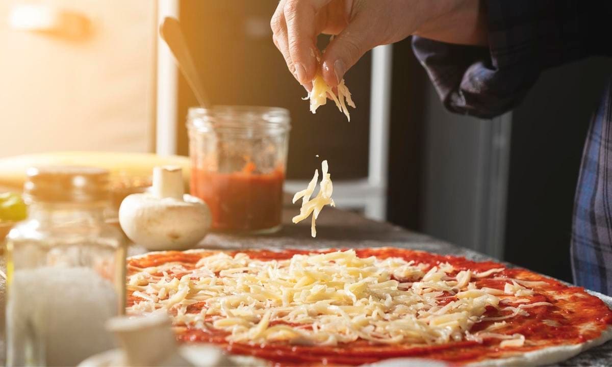 woman adding cheese on pizza