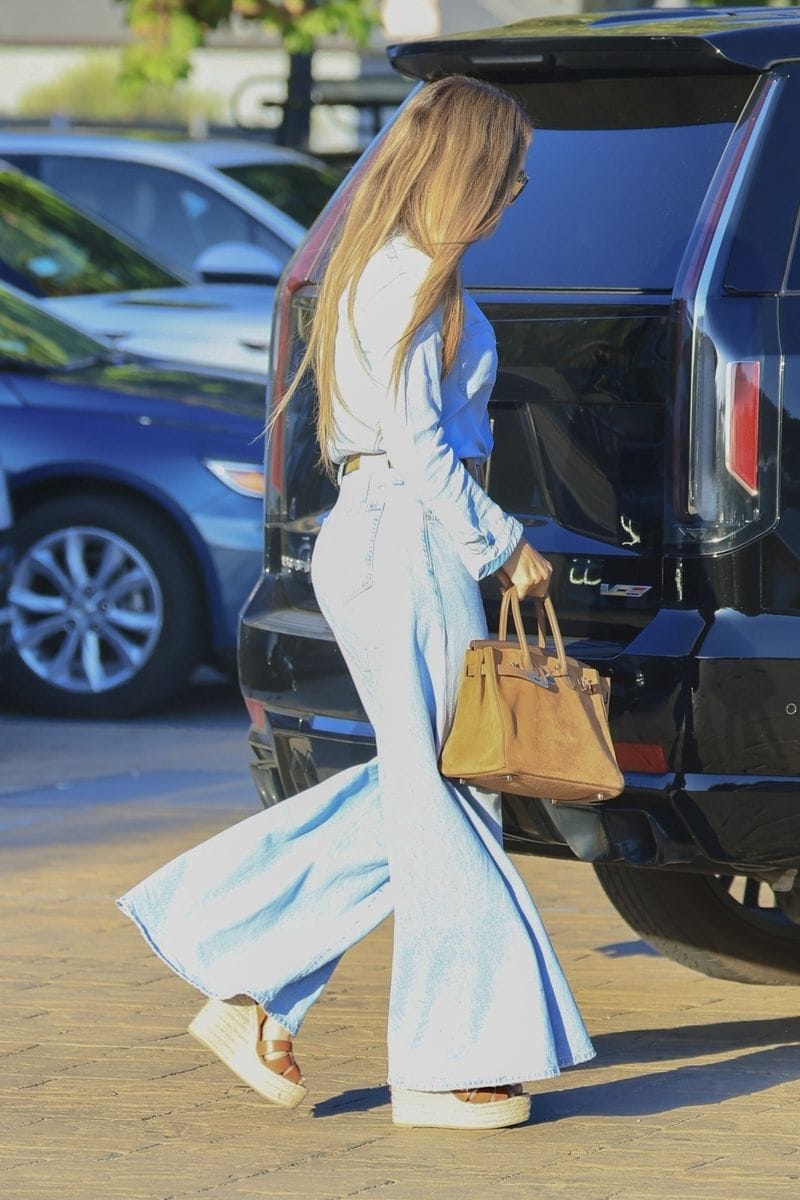 Jennifer Lopez wore a billowing denim-on-denim outfit with flowing jeans and a light-wash button up top, paired with wedge sandals.