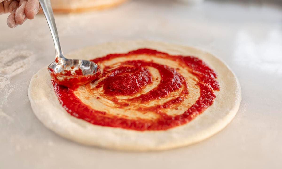 spreading tomato sauce on pizza pan