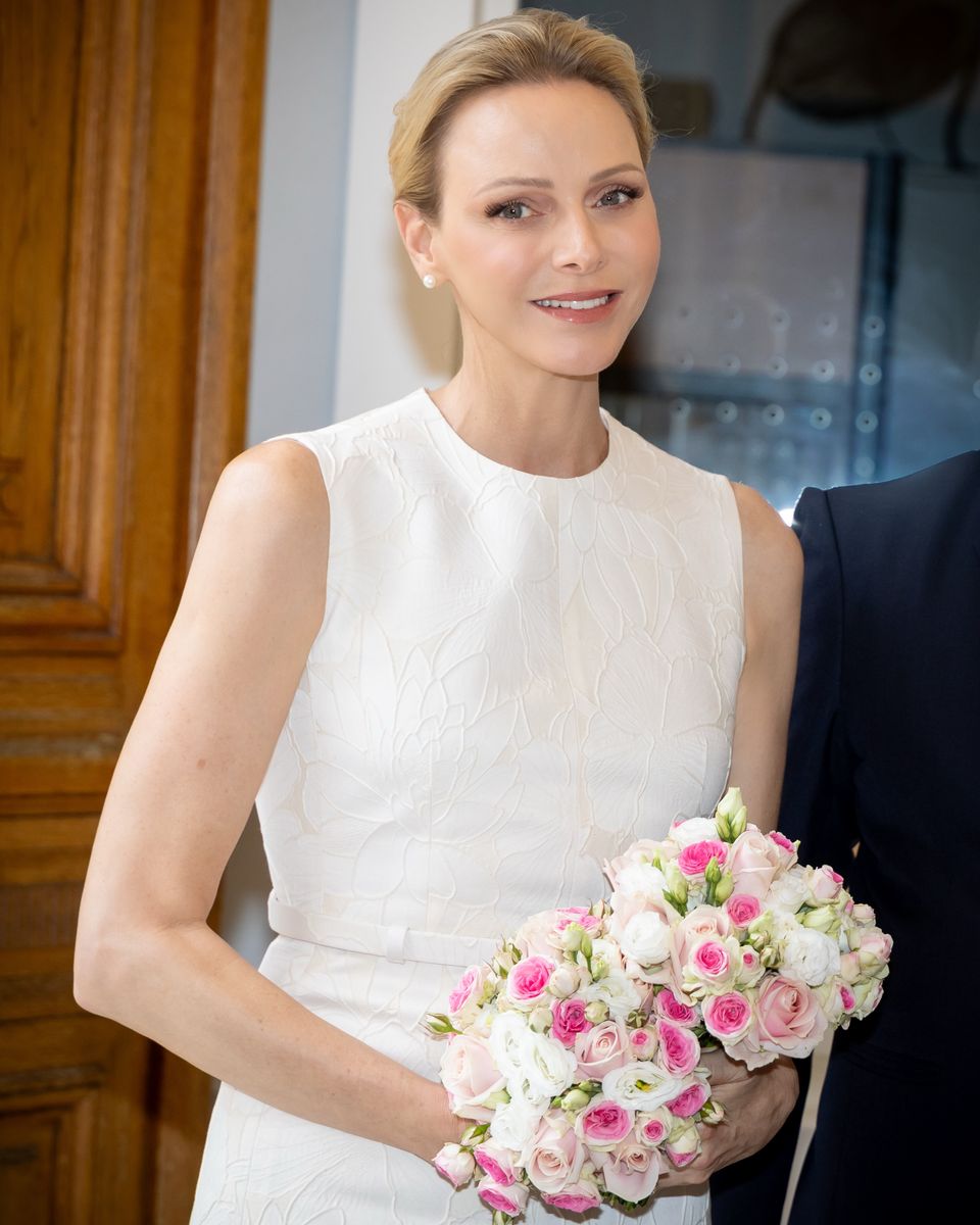 Charlene receives flowers from two young girls while wearing a white Carolina Herrera midi dress and neutral slingback heels.