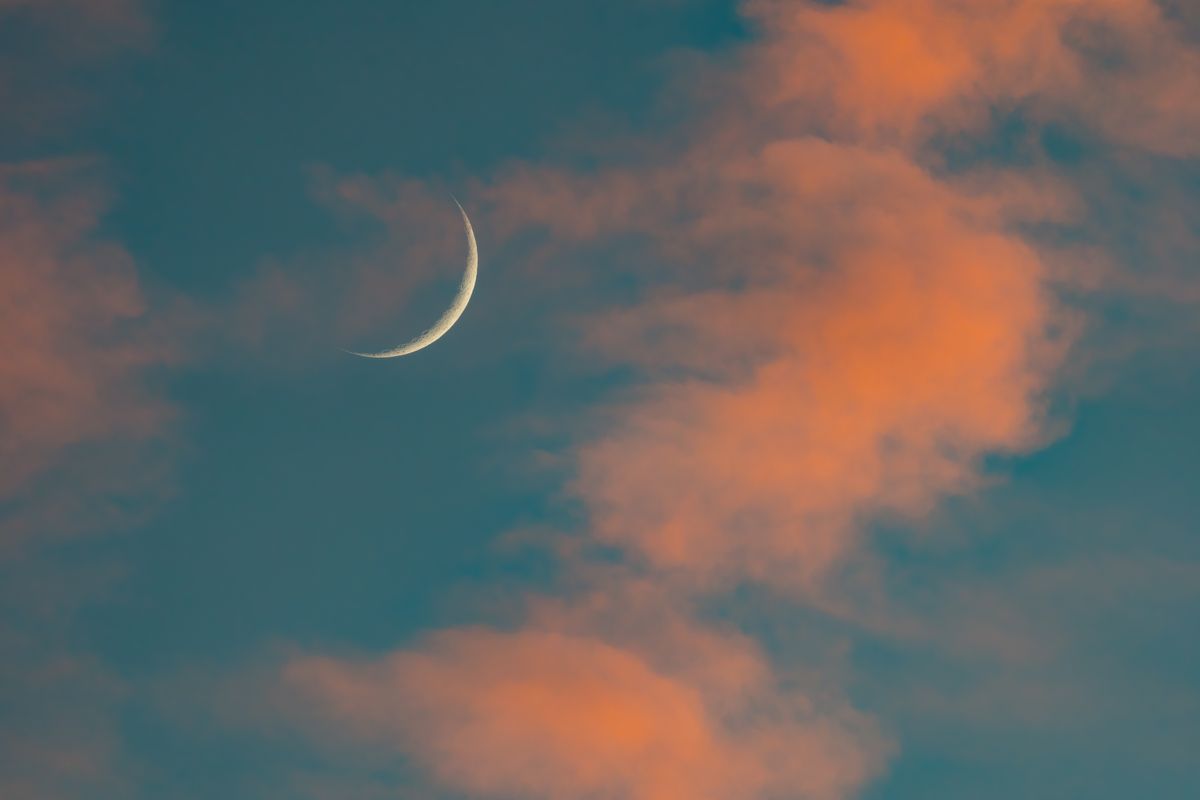 Crescent moon adorned by red clouds during a sunset.