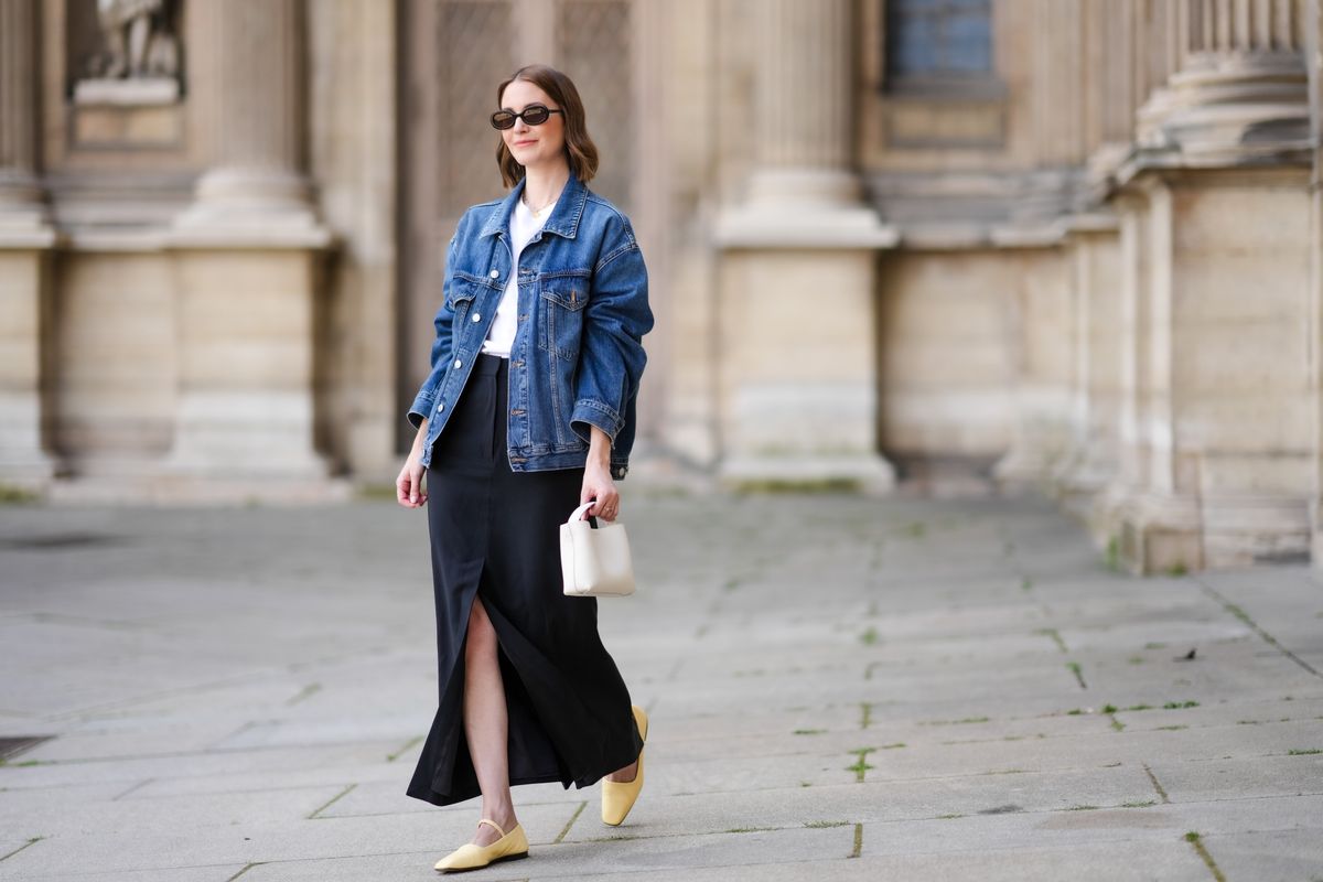 Marissa Cox wears an Arket black skirt, an Arket white T-shirt, a blue oversized Agolde denim jacket, ATP Atelier pale pastel yellow flats/shoes, a white Arket leather bag, Jimmy Fairly x Reformation sunglasses, and an Alighieri necklace during a street style fashion photo session on May 25, 2024, in Paris, France.