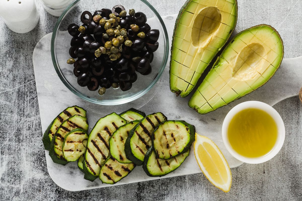Ingredients for a spring salad of ripe avocado, grilled zucchini, black olives, capers, and lemon dressing. This is a healthy vegan cuisine for the whole family or party.