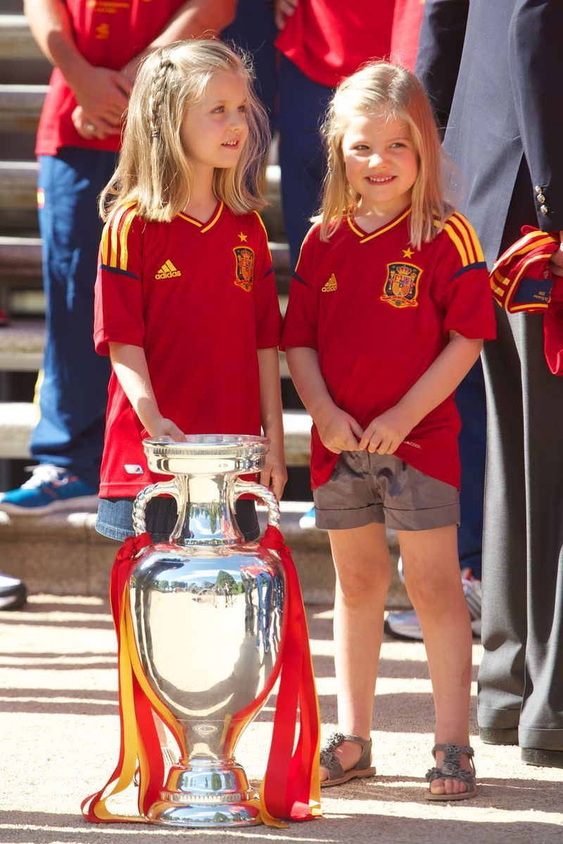 Princess Leonor of Spain and Princess Sofia of Spain stand next to the UEFA EURO 2012 trophy as King Juan Carlos I of Spain receives players of Spain's victorious national football team at Zarzuela Palace on July 2, 2012 in Madrid, Spain