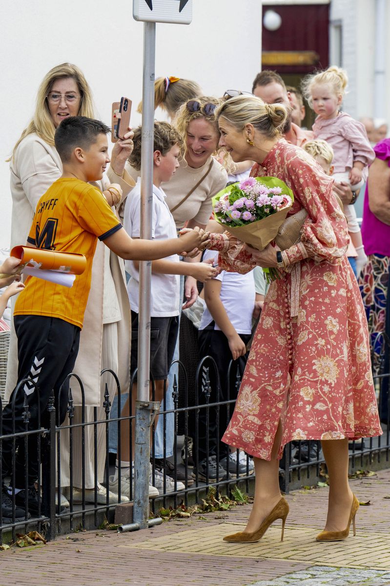 The queen pairs her floral midi dress with tan suede pumps, bringing a warm autumnal touch to the colorful look.