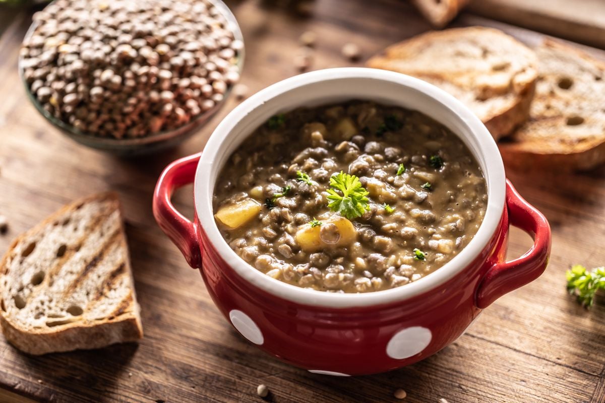 A bowl full of lentil legume soup with baked sausage and fresh bread.