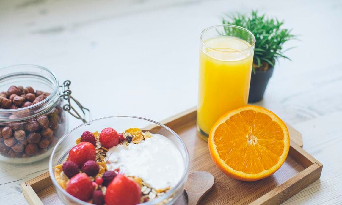 Bowl and jar with nuts, strawberries, and granola, and an orange half and orange juice