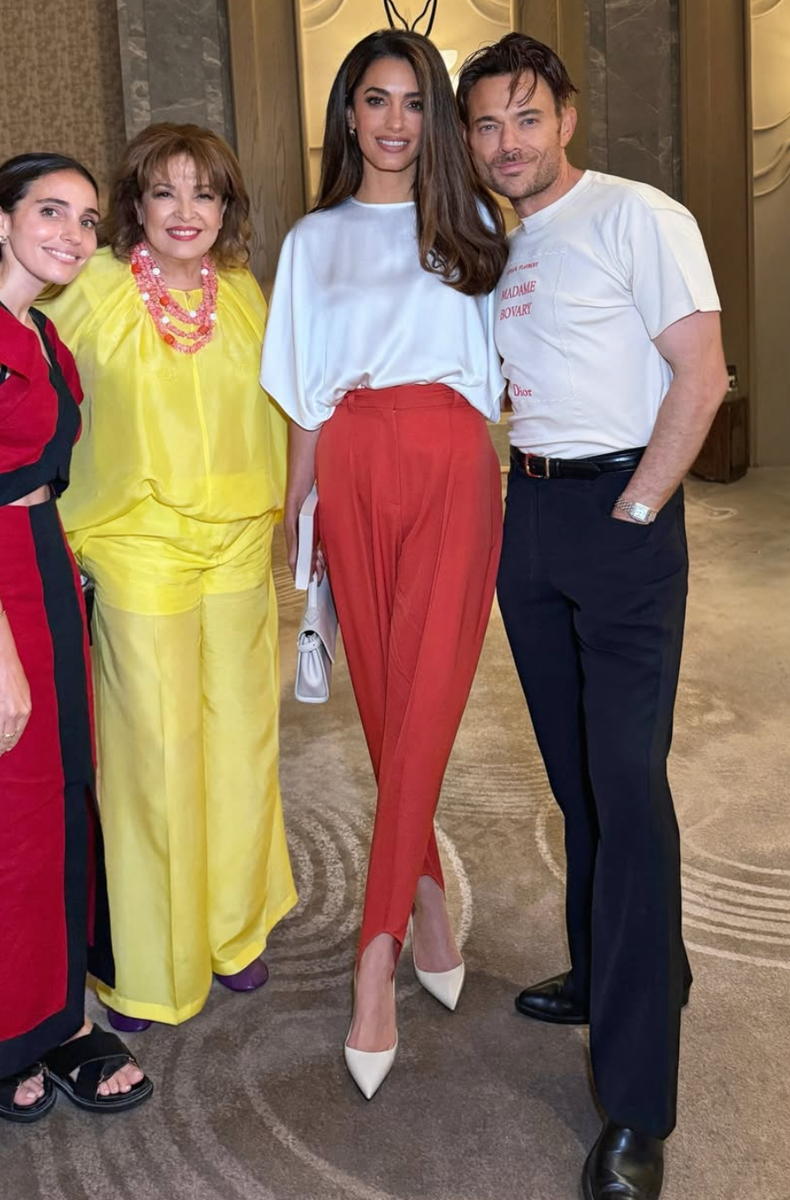 Amal’s flowing monochromatic white top allowed her glossy hair to take center stage, while the vibrant red-orange trousers created a fresh seasonal contrast.