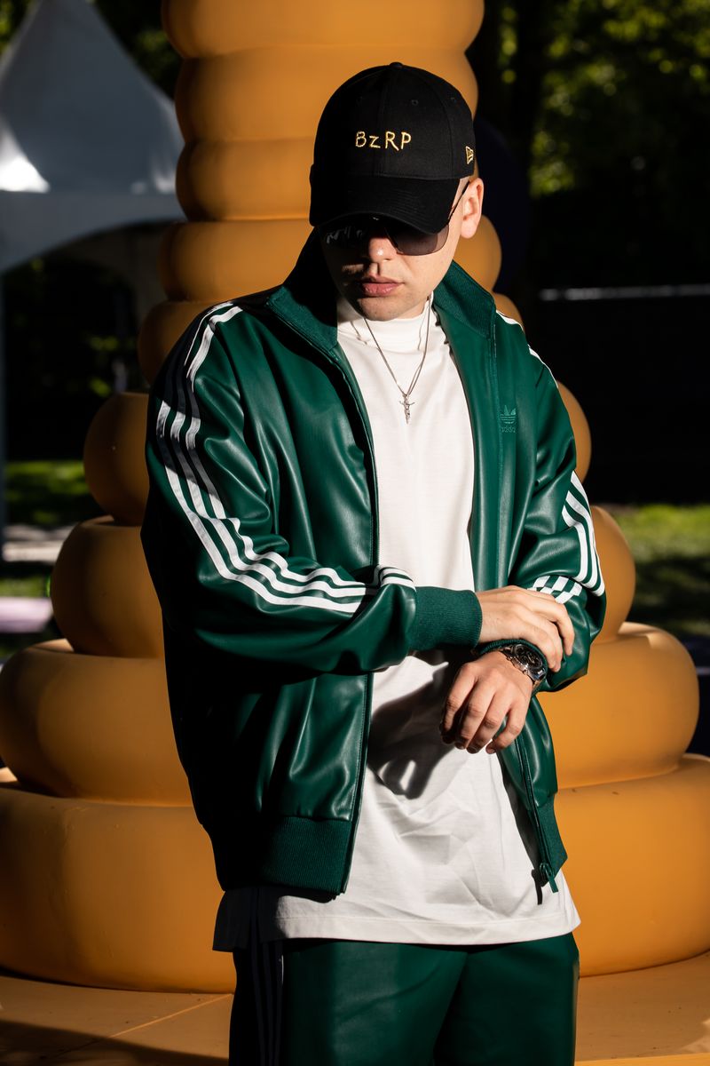 Person in green leather jacket and white shirt stands in front of yellow beehive structure.