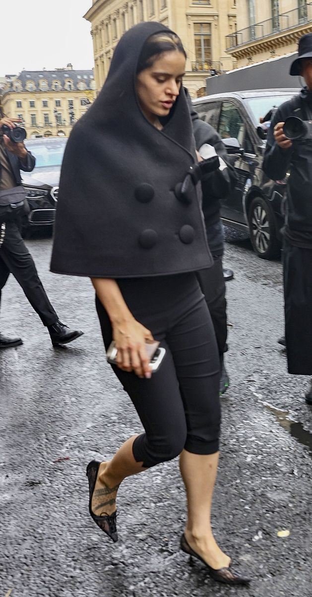Rosalía steps out in Paris wearing a charcoal hooded cape, black capri pants and pointed lace flats.