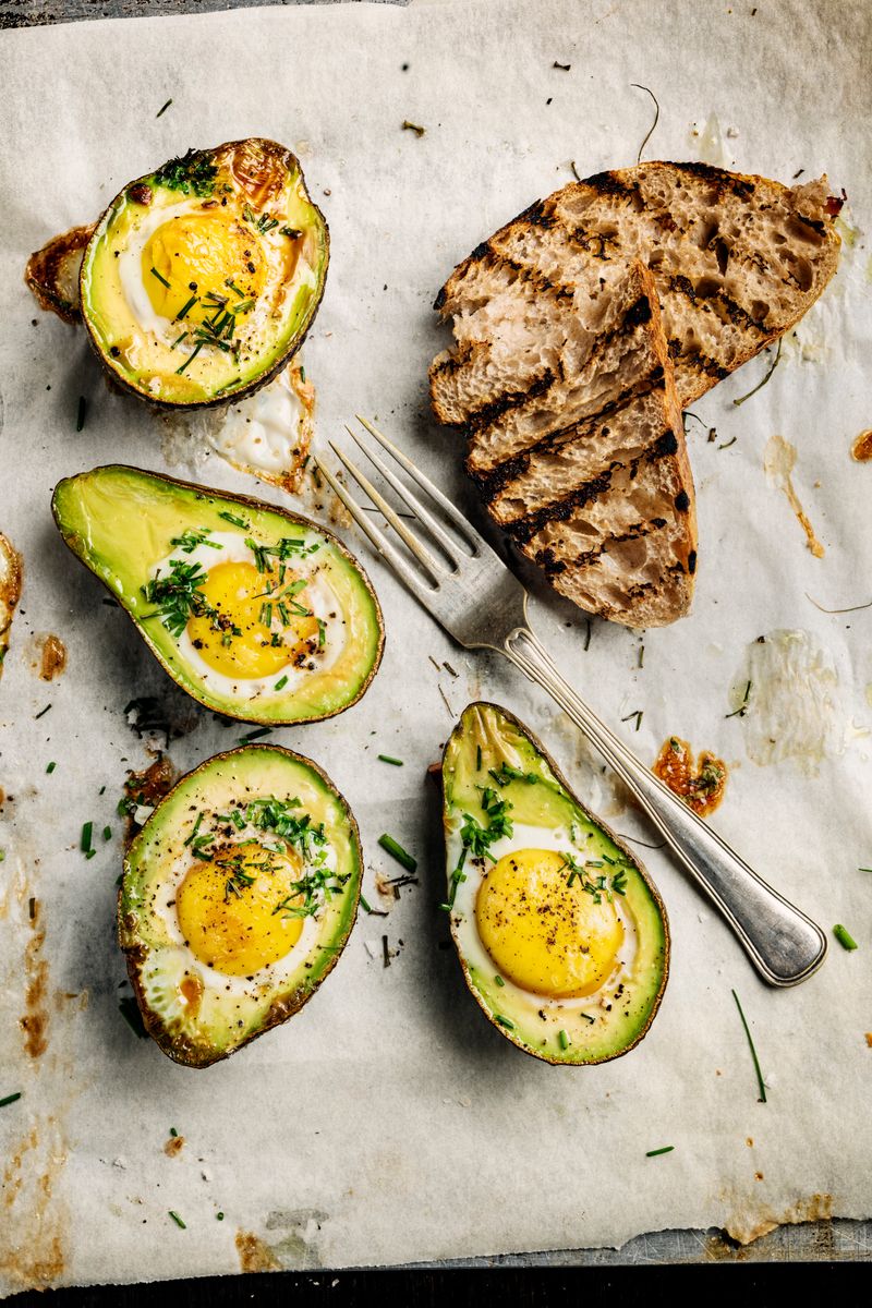 Overhead view of a dish of baked eggs with avocadoâs with toasted sourdough bread.