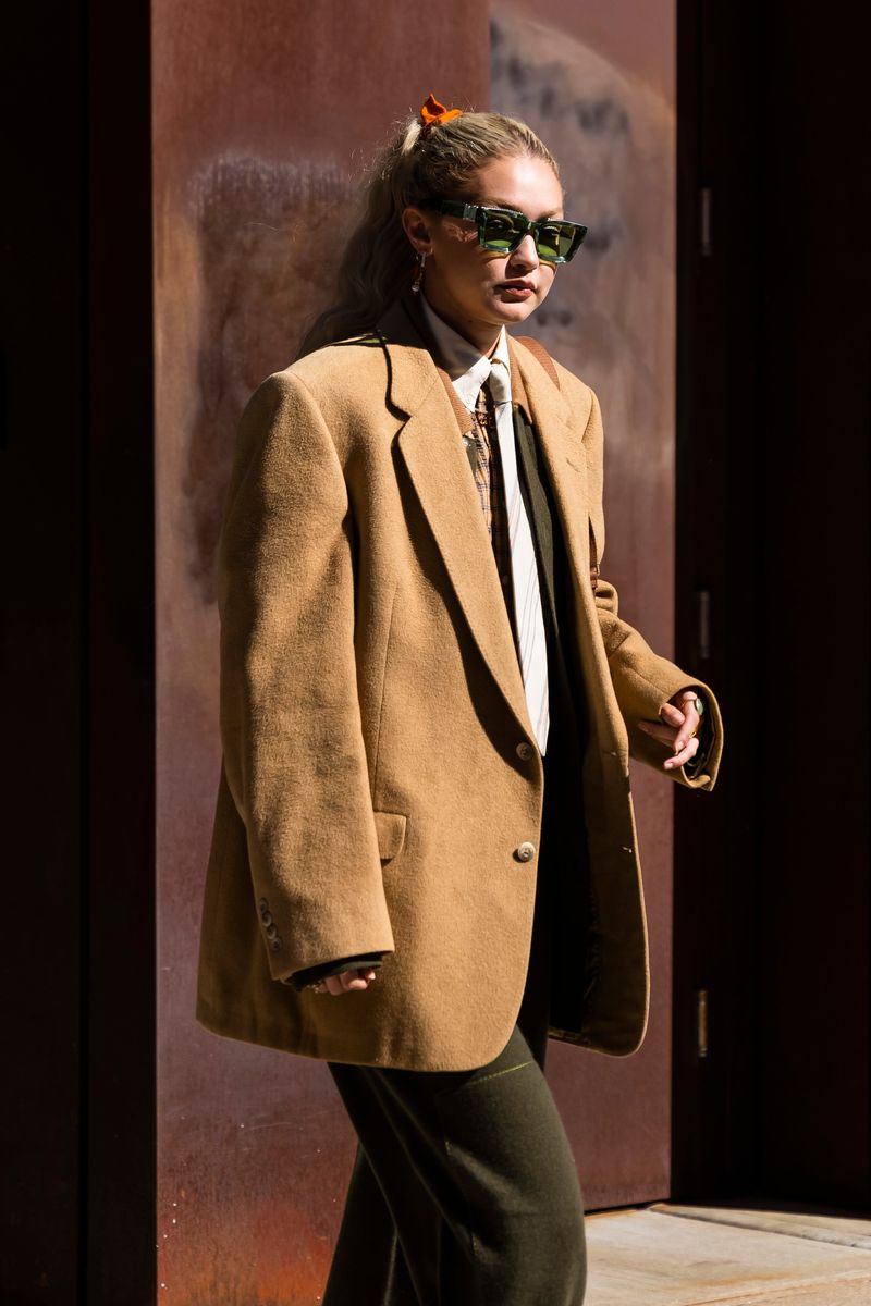 Gigi Hadid wearing a tailored jacket combined with green glasses and hair tied back.