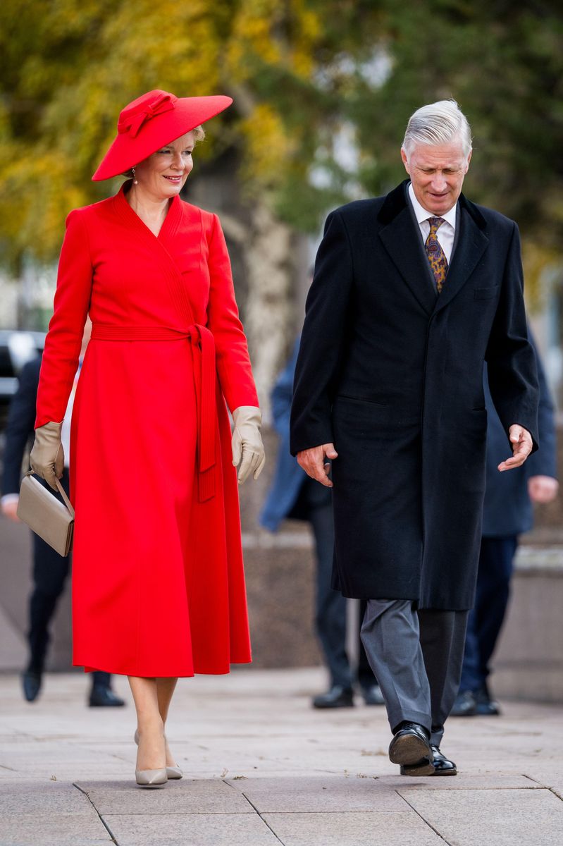 Queen Mathilde pairs her vibrant red midi dress with coordinating taupe gloves, a structured handbag and pointed-toe pumps.
