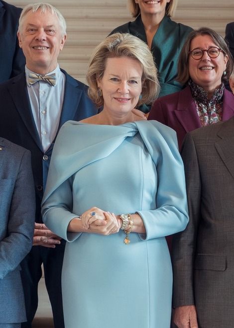 Queen Mathilde embraces modern royal elegance in a sophisticated pastel-blue ensemble, pairing her statement dress with neutral pointed-toe heels and delicate jewelry.
