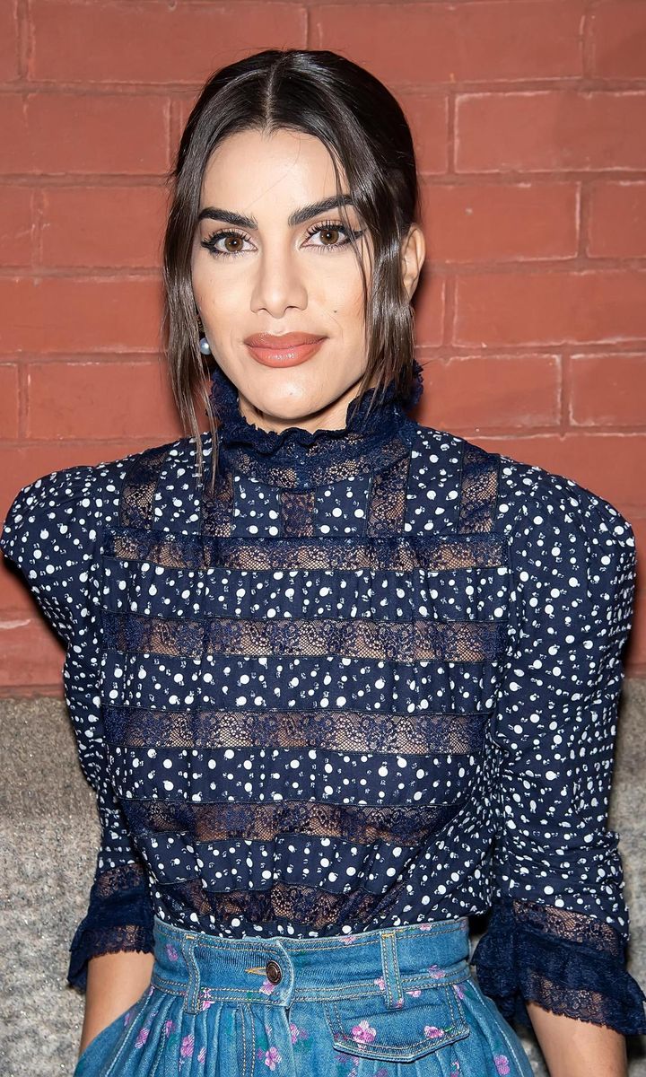 Camila Coelho wearing a blouse with sheer strips, her hair up, and two wisps of hair to frame her face