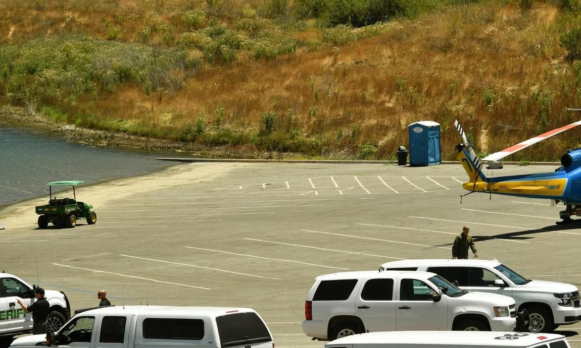 Sheriff department vehicles and a helicopter sit in a parking lot along with emergency workers at Lake Piru