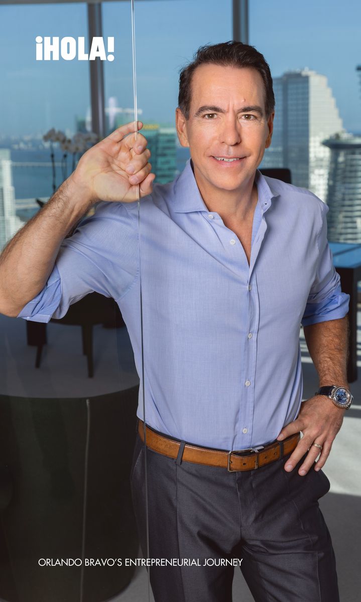 hile leaning against a glass partition in his Miami office, with a panoramic city view in the background.
