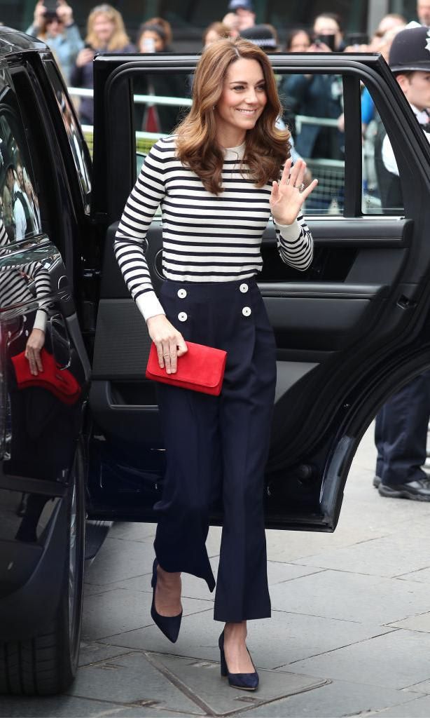 Kate Middleton wearing high-rise pants with a wide leg, matching navy blue striped sweater, red clutch, and suede stilettos