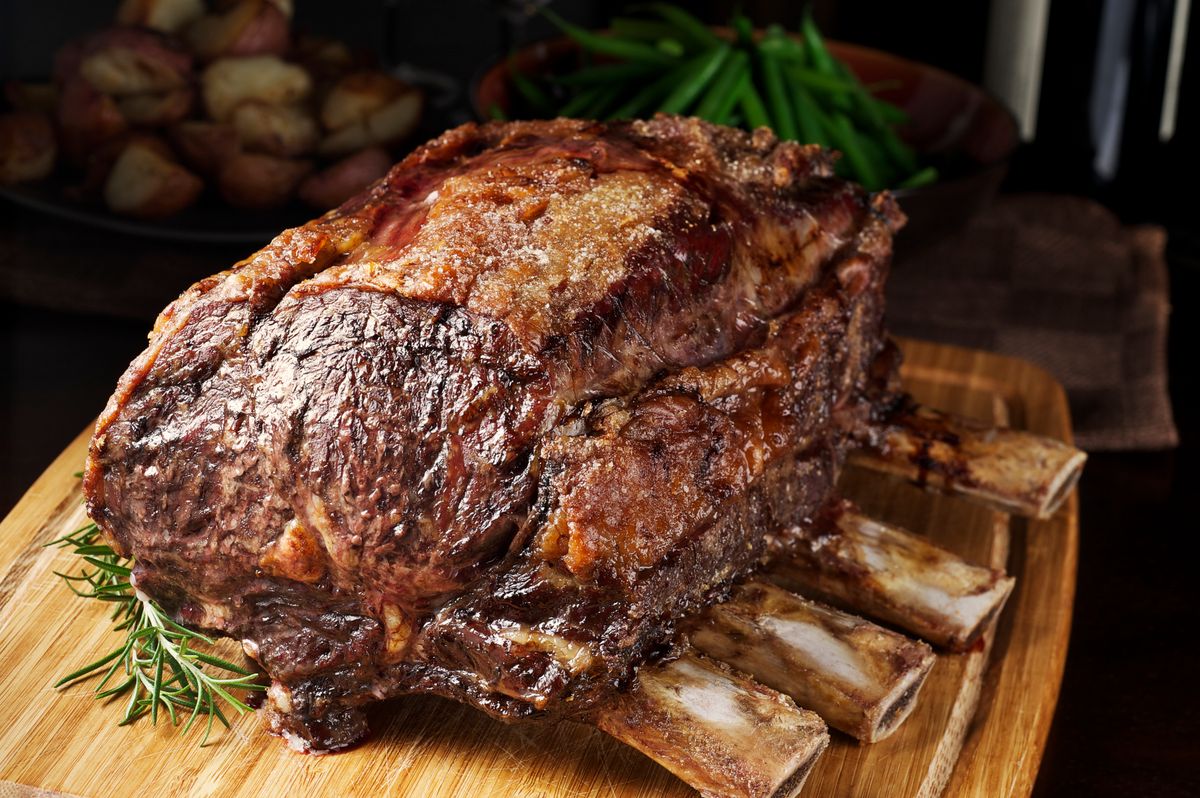 "SEVERAL MORE IN THIS SERIES. Roasted prime rib, hot from the oven, dripping juices, and ready to be carved.  Also known as a standing rib roast; this is the cut from which ribeye steaks are made.  Potatoes, green beans and wine bottle in the background.  Shallow DOF." 