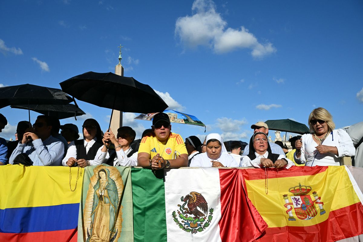 People stand next to flags of Colombia, Mexico and Spain as they gather at St Peter's Square on the second day of the conclave in the Vatican on May 8, 2025. 