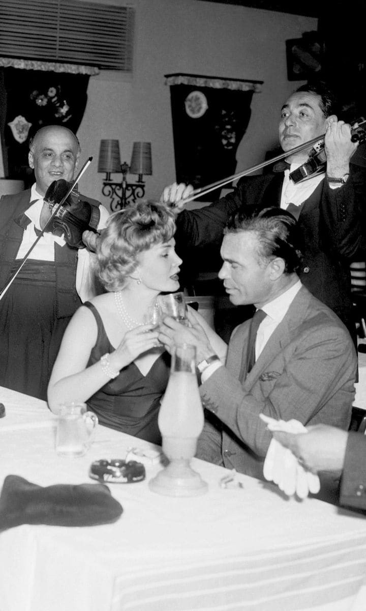 Porfirio Rubirosa and Zsa Zsa Gabor toast each other while m