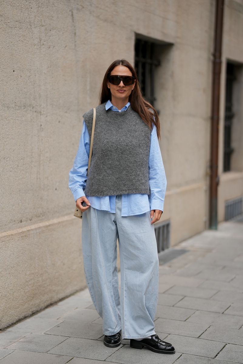 Anna Winter is seen wearing a gray wool sleeveless sweater vest from Black Palms over a light blue cotton shirt from Mother; light blue wide-leg trousers from Agolde; black leather loafers from Prada