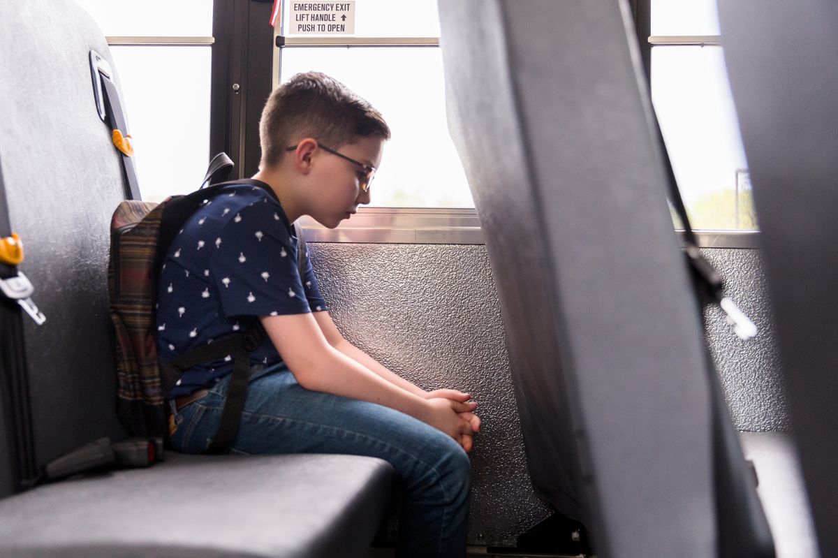 Elementary school boy sits alone on a school bus, looking sad.