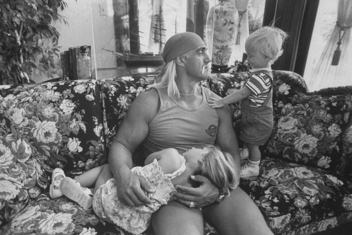 Wrestler Hulk Hogan cuddling w. his 3-yr-old daughter Brooke as he chats w. his 1-yr-old son Nicholas while relaxing together on a floral print couch at home.  (Photo by Acey Harper/Getty Images)