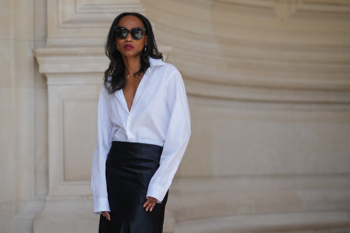 Emilie Joseph wears sunglasses from Gentle Monster, earrings, red lipstick, make-up, a white oversized poplin button-down shirt from Figaret Paris, and a long maxi silk lustrous skirt in black during a street style fashion photo session on May 20, 2024, in Paris, France. (Photo by Edward Berthelot/Getty Images)