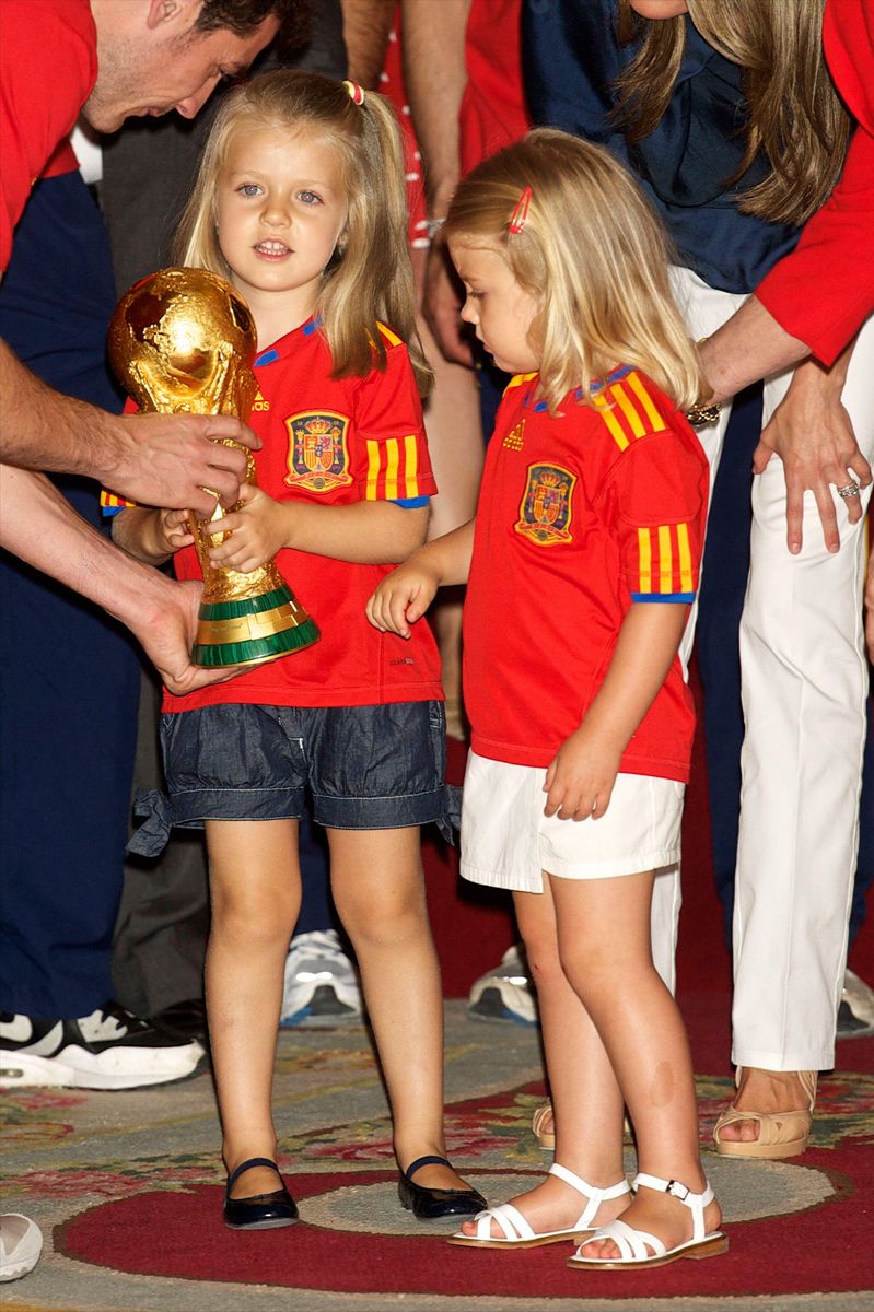 Princess Leonor and Infanta Sofía, dressed in matching Spain jerseys, share a magical moment with football's most coveted prize.