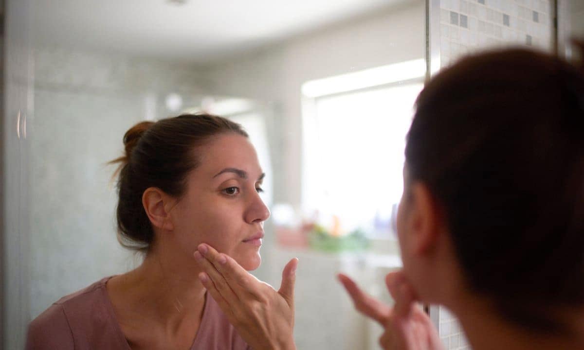Young female in the bathroom looking in the mirror and taking care of her facial skin.