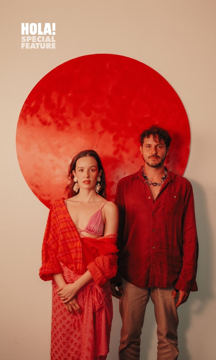 A man and a woman stand together in front of a red circular backdrop.