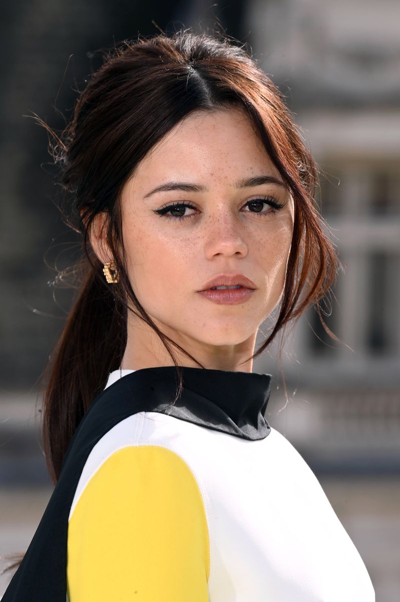 A softly styled ponytail, winged eyeliner and gold earrings complete Ortega’s photocall look.