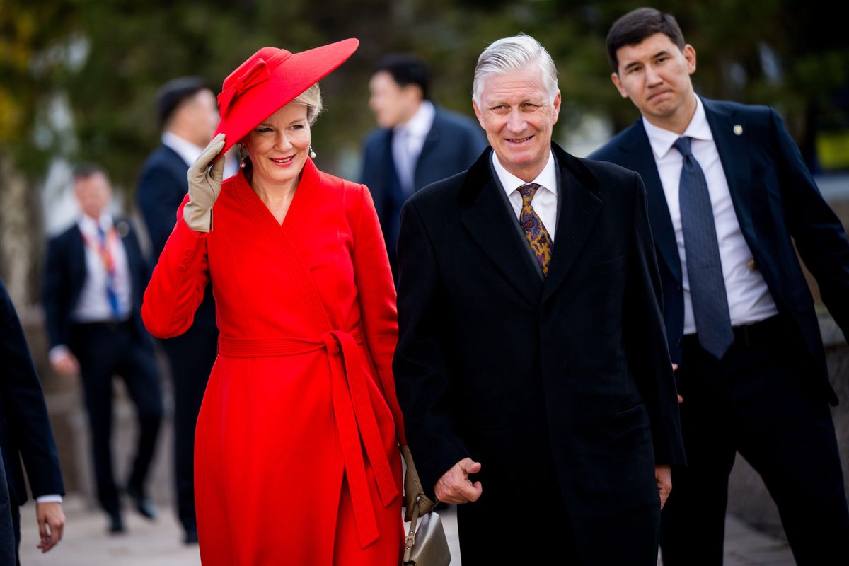 Queen Mathilde adjusts her wide-brimmed red hat while walking alongside King Philippe in Astana.