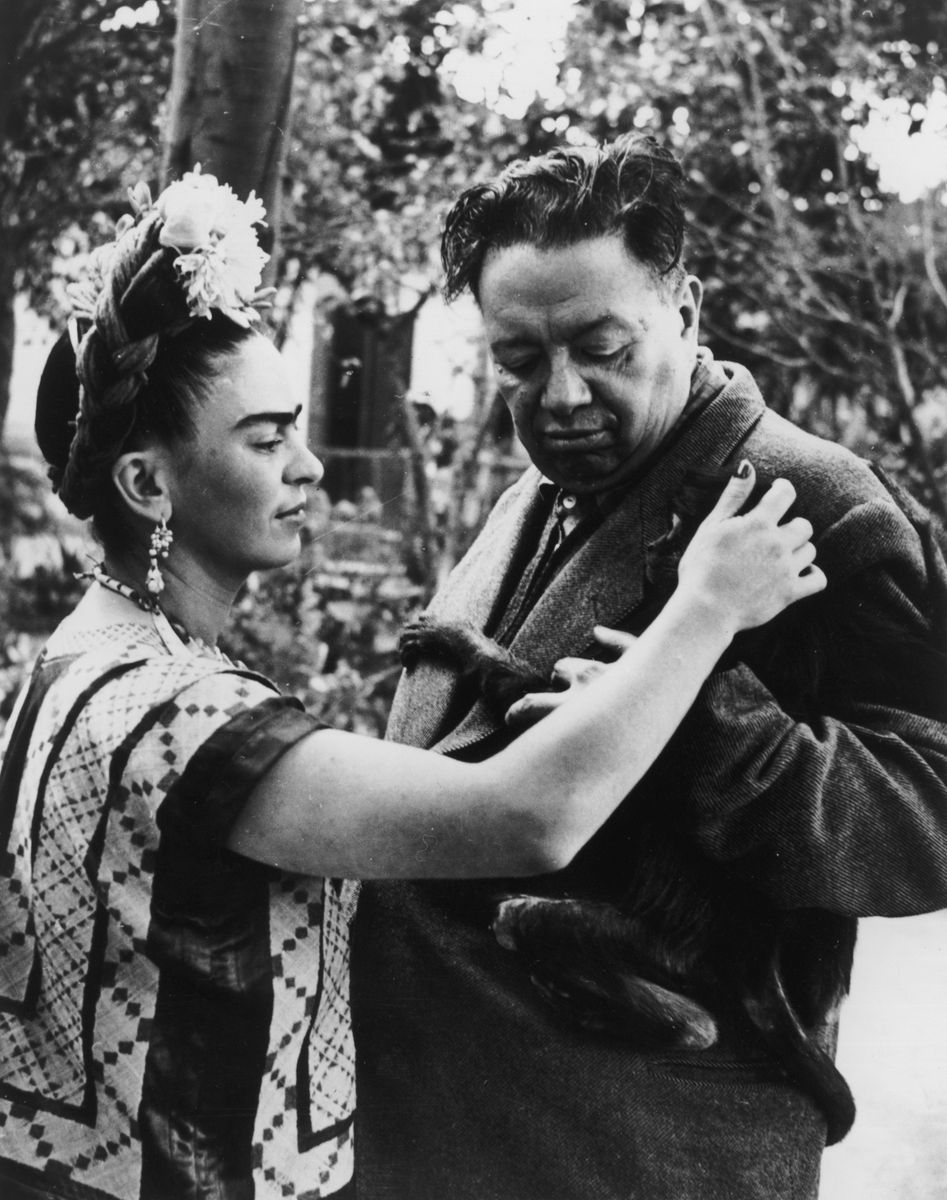 Mexican artist Frida Kahlo (1907 - 1954) pets a monkey, possibly Fulang-Chang, clinging to the jacket of her husband, Mexican artist Diego Rivera (1886 - 1957).  