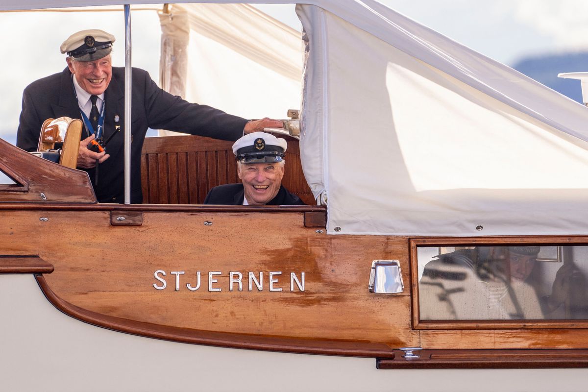 King Harald V of Norway smiles during the traditional H.M. Kongens Serieseilaser regatta in the Oslofjord on June 11, 2024, alongside Peter T.M. Brandt, secretary general of the Royal Norwegian Yacht Club.