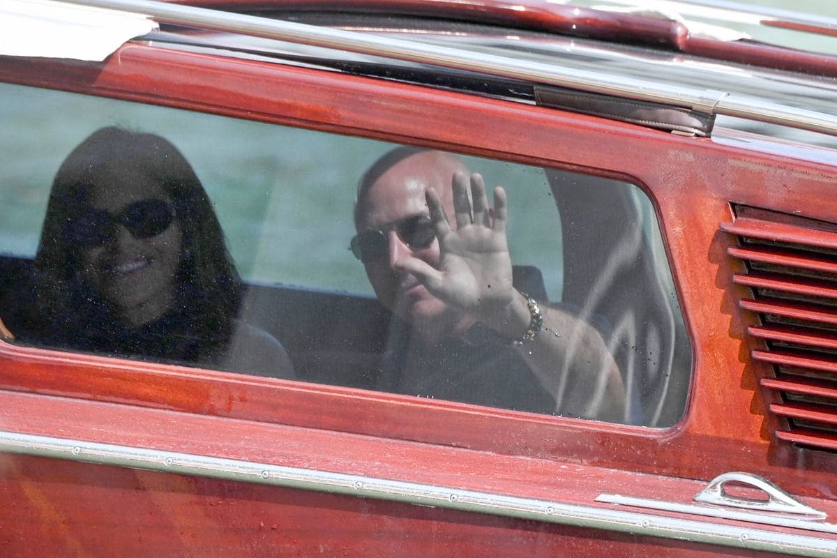 Jeff Bezos and Lauren Sanchez wave from the taxi-boat as they arrive at the Aman Hotel on June 25, 2026. 
