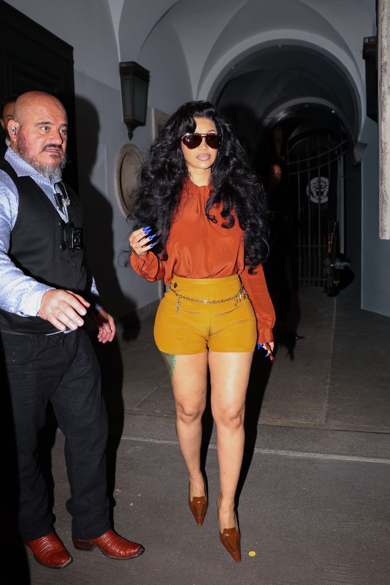 Cardi B steps out in Milan in mustard shorts, an orange blouse and brown heels after taking the Vogue World runway in archival Versace during Fashion Week.