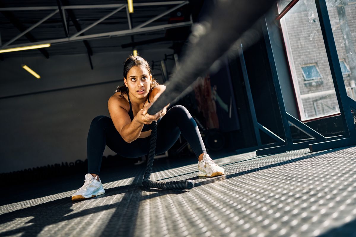 Female athlete pulling a weighted sled in a gym. Front view of a woman performing strength training exercise on a black gym floor. Hyrox Training Concept.