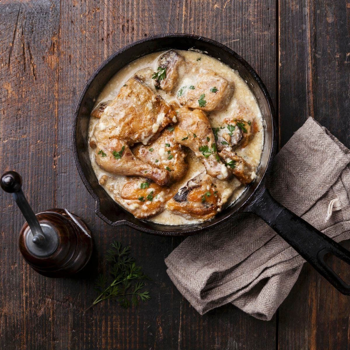 Roasted chicken with creamy garlic sauce in cast iron frying pan on dark wooden background