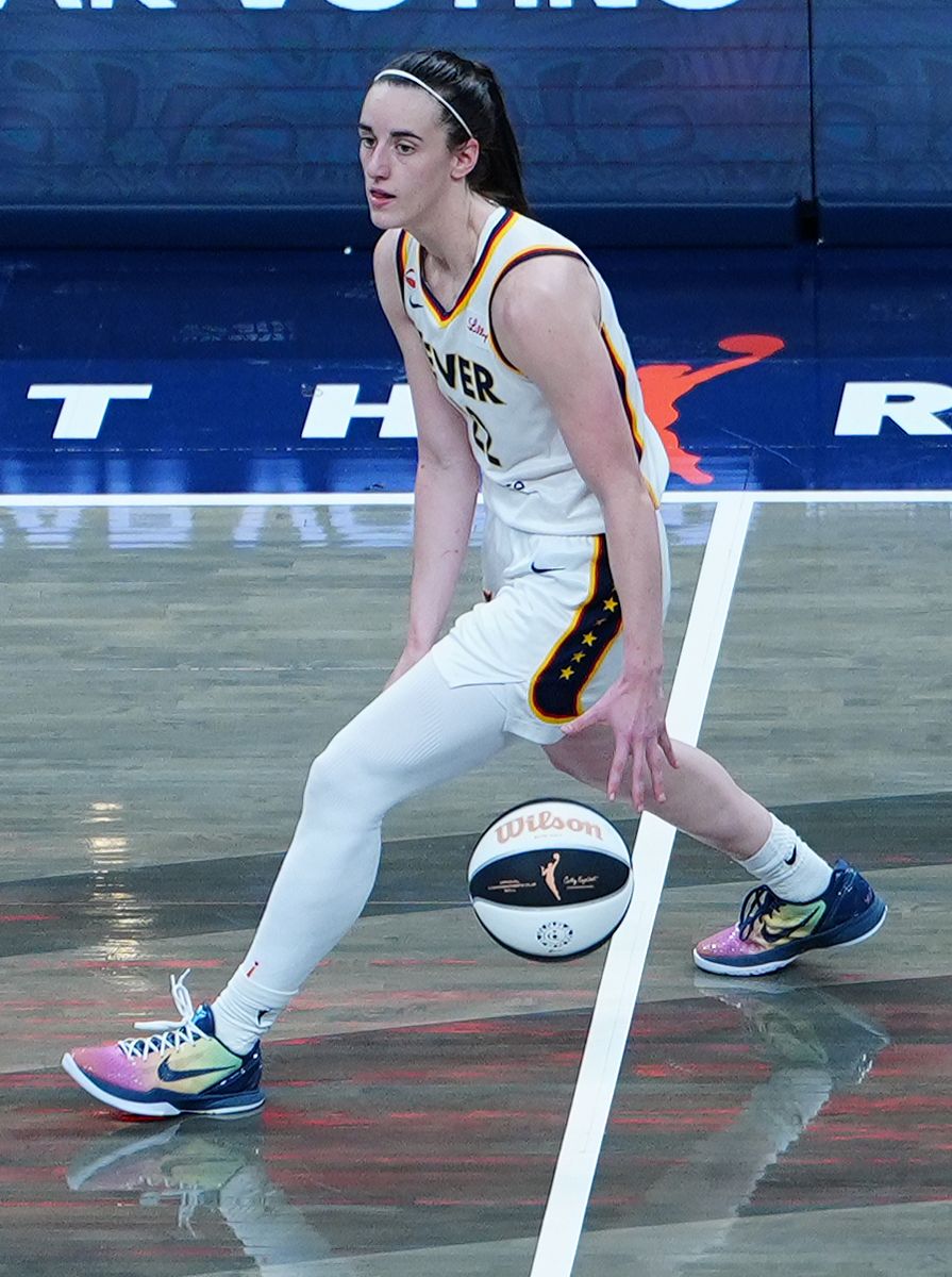 Indiana Fever guard Caitlin Clark (22) dribbles between her legs wearing her Taylor Swift themed shoes, the NIKE 6 Protro "Eras Tour"